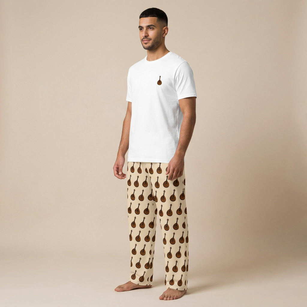 Male model wearing a white T-shirt with a small oud motif and cream wide-leg pants patterned with brown oud instruments.