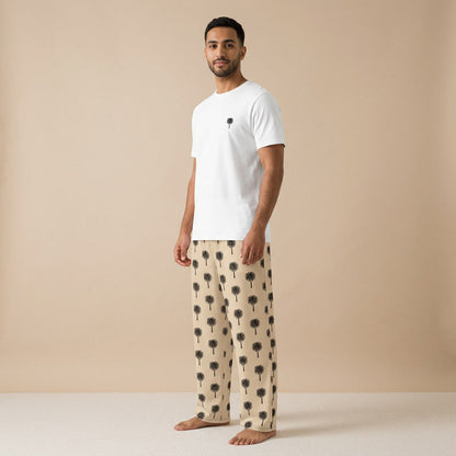 Male model wearing a white T-shirt with a small black palm tree on the chest and beige wide-leg pants with a black palm tree pattern.