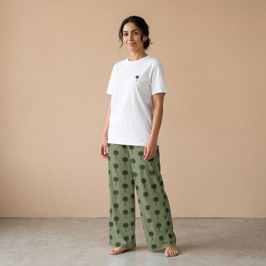 Model wearing a white T-shirt with a small palm tree motif and olive green pants with black palm tree prints, front view.