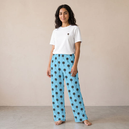 Model wearing a white T-shirt with a small palm tree motif and light blue pants with black palm tree prints, front view.