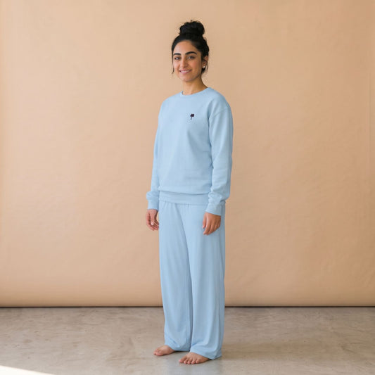 Model wearing a light blue sweatshirt with a small palm tree chest motif and matching wide-leg pants.