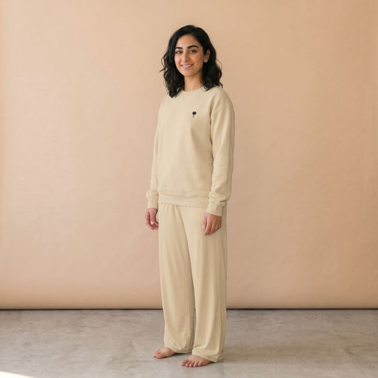 Model wearing a sand-coloured sweatshirt with a small palm tree chest motif and matching wide-leg pants.