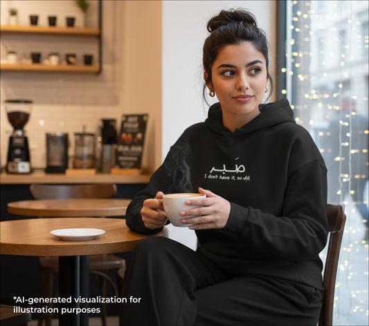 Woman in a black hoodie holding a steaming cup of coffee in a cafe setting.