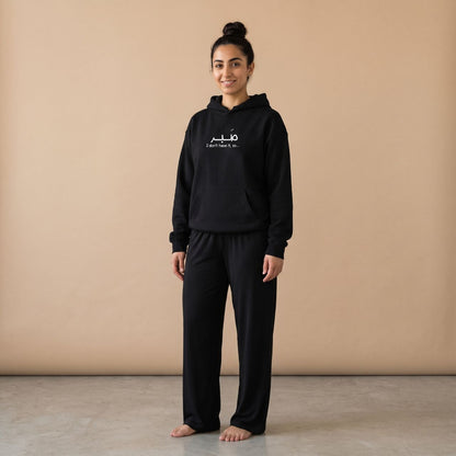 Model wearing a black hoodie with “صبر” and “I don’t have it, so…” text and plain black wide-leg pants, front view.