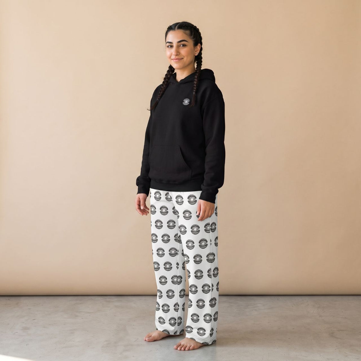 Model wearing a black hoodie with a small pearl shell motif and white pants with black pearl shell prints, front view.