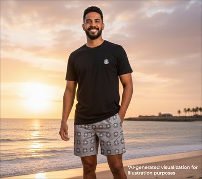Man standing on a beach at sunset wearing a black t-shirt and pearl patterned shorts.