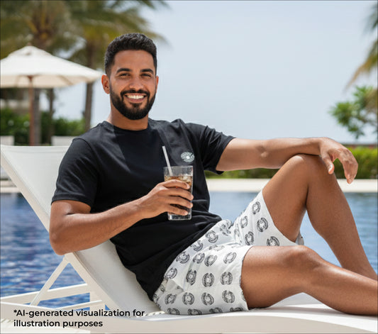 Man lounging by a pool holding a drink wearing a black t-shirt with a small pearl print and pearl patterned swim trunks.