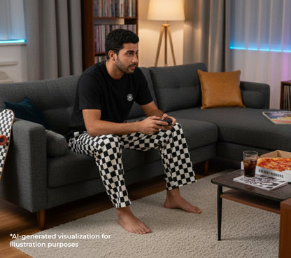 Man sitting on a couch holding a gamestick wearing a black t-shirt with a small print print and checkered black and white pants