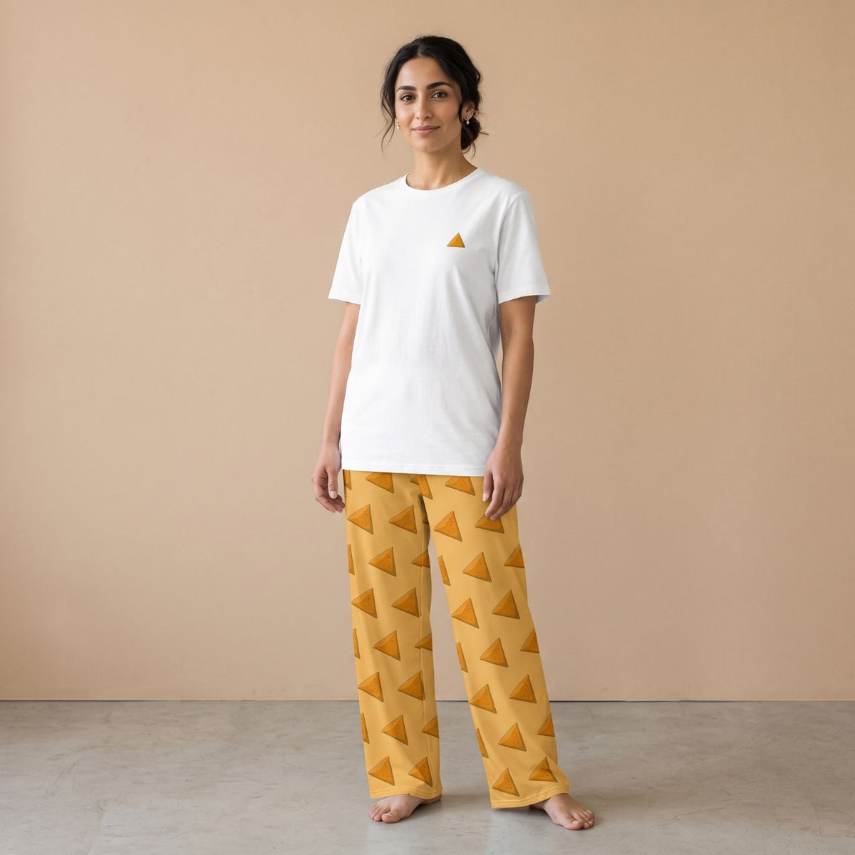 Model wearing a white T-shirt with a small samosa motif and golden yellow pants with an all-over samosa print, front view.