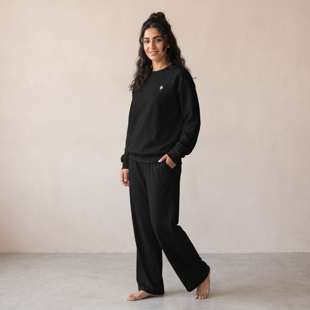 Model wearing a black sweatshirt with a small white palm tree chest motif and matching wide-leg pants.