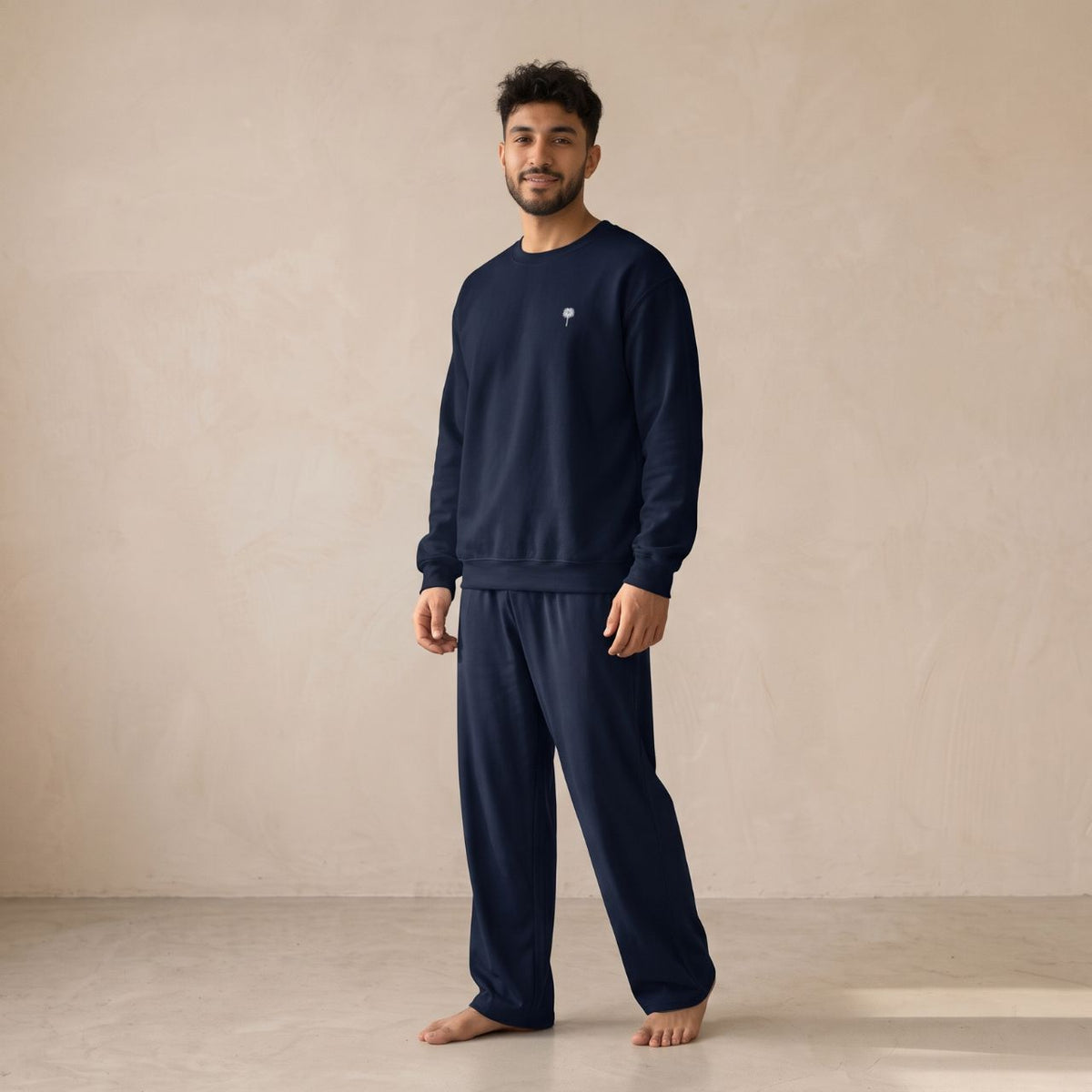 Model wearing a navy sweatshirt with a small white palm tree chest motif and matching wide-leg pants.