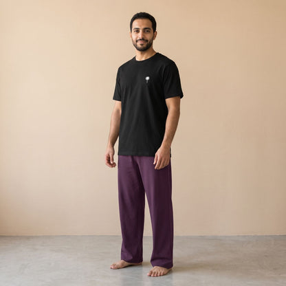 Model wearing a black T-shirt with a small white palm tree motif and plain purple pants, front view.